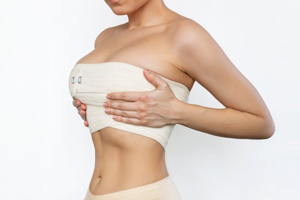 Young woman holds her chest, wrapped in bandages, after a breast lift